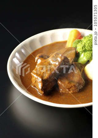 ブロッコリー、人参、ジャガイモが付け合わせてある厚切り牛タンの熱々ビーフシチューを黒背景で撮影 105071305