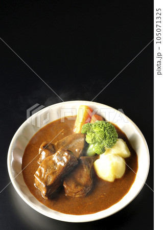 ブロッコリー、人参、ジャガイモが付け合わせてある厚切り牛タンの熱々ビーフシチューを黒背景で俯瞰撮影 105071325