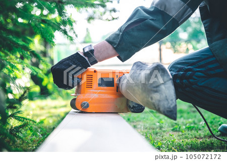 The man grinds the boards with a belt grinder, the electric tool for grinding and polishing the surface of the wooden board. 105072172