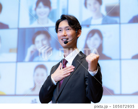 ホールで観衆とテレビ電話でつながっている人物を相手に講演をする男性講師 ホールで観衆とテレビ電話でつながっている人物を相手に講演をする男性講師 105072935