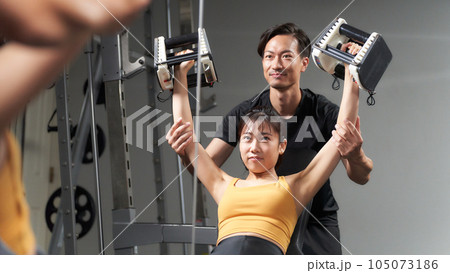ジムでトレーニングをする女性とサポートするトレーナー ジムでトレーニングをする女性とサポートするトレーナー 105073186