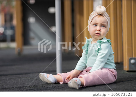 Concerned toddler girl sitting on sunlit playground surface Concerned toddler girl sitting on sunlit playground surface 105073323