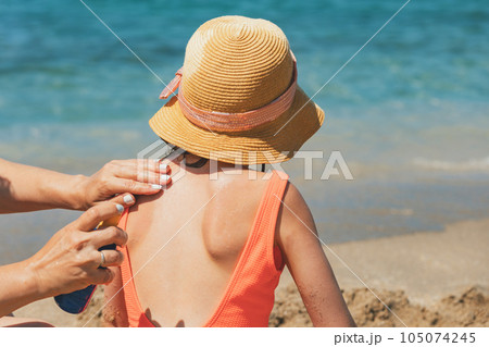 Mother applying sunscreen spray to her child at a beach Mother applying sunscreen spray to her child at a beach 105074245