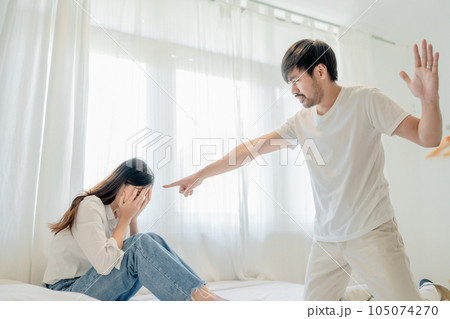 Domestic Violence, Asian Husband Threatening Wife, Scared Mother Embracing is her While Sitting Together On bed Domestic Violence, Asian Husband Threatening Wife, Scared Mother Embracing is her While Sitting Together On bed 105074270