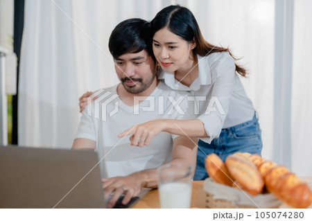 Happy young loving family couple looking at laptop computer screen, reading ecipes. Wife showing embrace to husband to pretty joyful husband, sitting at table in kitchen at home in weekend Happy young loving family couple looking at laptop computer screen, reading ecipes. Wife showing embrace to husband to pretty joyful husband, sitting at table in kitchen at home in weekend 105074280