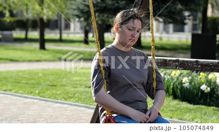 Adult woman riding swing sits with upset expression in park Adult woman riding swing sits with upset expression in park 105074849