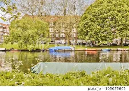 boats on the water in front of an apartment building with trees and grass around it is clear blue sky above 105075693