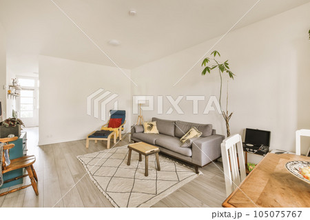 a living room with white walls and wood flooring in the center of the room, there is a grey couch 105075767
