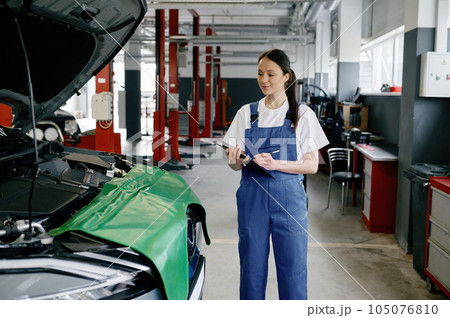 Young woman mechanic writing on clipboard at repair garage Young woman mechanic writing on clipboard at repair garage 105076810