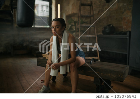Relaxed woman boxer resting on bench with towel on neck Relaxed woman boxer resting on bench with towel on neck 105076943