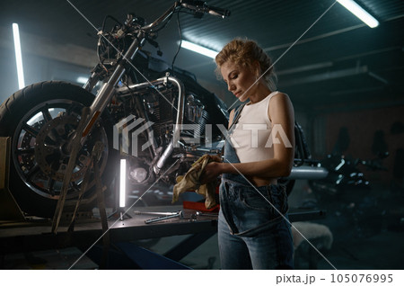 Young woman motorcycle engineer repairing bike at workshop in evening Young woman motorcycle engineer repairing bike at workshop in evening 105076995
