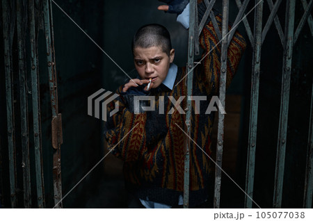 Unhappy depressed woman beggar with smoldering cigarette behind bars Unhappy depressed woman beggar with smoldering cigarette behind bars 105077038