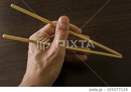 The left hand of a man using bamboo chopsticks on a wooden background The left hand of a man using bamboo chopsticks on a wooden background 105077129