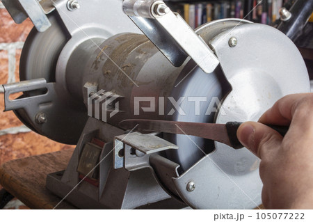 Knife sharpener and hand with blade on wooden table, closeup 105077222