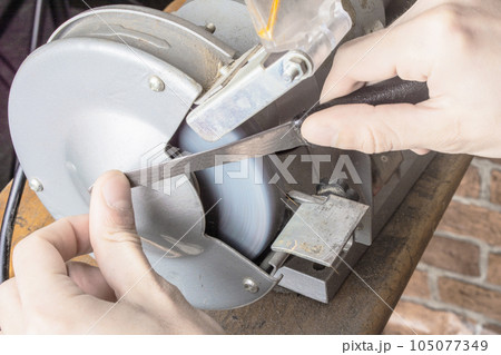 Knife sharpener and hand with blade on table, closeup Knife sharpener and hand with blade on table, closeup 105077349