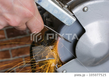 Knife sharpener and hand with blade on wooden table, closeup 105077525