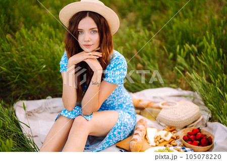 Young woman sits on a plaid with a book. Summer picnic in nature. Healthy food. Young woman sits on a plaid with a book. Summer picnic in nature. Healthy food. 105078220