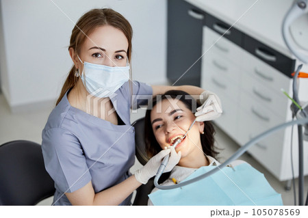 Beautiful young woman doing tooth examination in the dental office. Portrait of smiling girl on a dental chair in dentistry 105078569