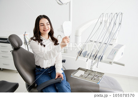 Happy woman patient checking teeth in mirror. Female at the dentist office 105078570