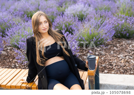 Pregnant woman sits on bench in the park holding cup of coffee Pregnant woman sits on bench in the park holding cup of coffee 105078698