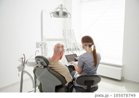 Portrait of young female dentist standing by mid adult man in clinic. Female dentist repairing patient tooth in dental ambulant 105078749