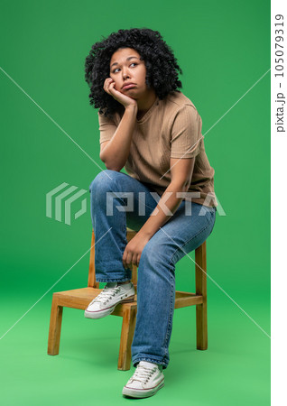 Dark-haired young woman sitting on the chair and looking upset 105079319