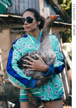 Stylish young woman farmer holds goose. 105079512
