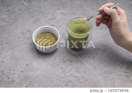 Human hand Adds Spoon of Hemp Protein Powder To Glass With Smoothie, Juice. Drink With Plant-derived Protein from Cannabis Plant. Superfood, Healthy Lifestyle. Horizontal Plane Human hand Adds Spoon of Hemp Protein Powder To Glass With Smoothie, Juice. Drink With Plant-derived Protein from Cannabis Plant. Superfood, Healthy Lifestyle. Horizontal Plane 105079846