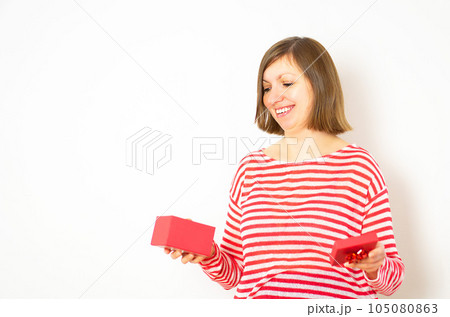 Portrait of happy beautiful woman in white and red shirt opening a red present box and smile. Portrait of happy beautiful woman in white and red shirt opening a red present box and smile. 105080863