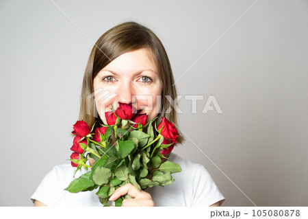 A portrait of an attractive smiling girl with a bouquet of red roses in the hands. A portrait of an attractive smiling girl with a bouquet of red roses in the hands. 105080878