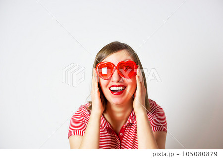 Valentines Day portrait of pretty smiling woman in red sunglasses on the white background. Valentines Day portrait of pretty smiling woman in red sunglasses on the white background. 105080879