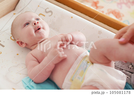 4 months old infant boy lying on changing desk, mother hands holding his legs 105081178