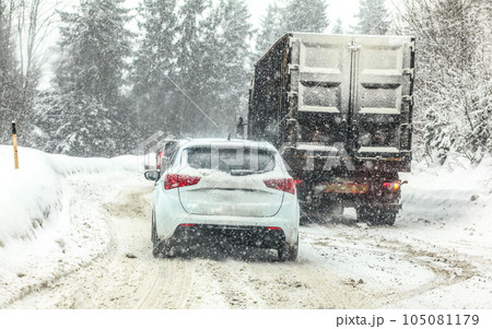 Traffic jam on forest road, cars and trucks moving slowly - mountain pass during heavy snow blizzard 105081179
