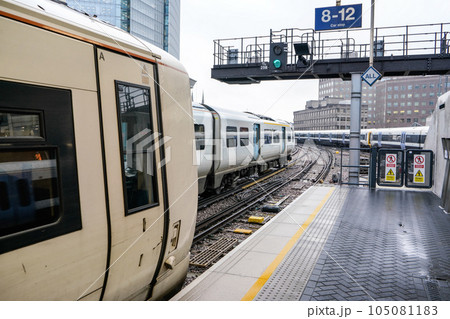 Empty platform at London Bridge station, multiple trains on rail tracks, tall buildings background during overcast day 105081183