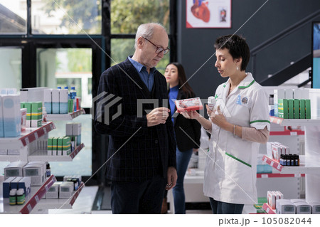 Elderly man buying supplements and getting heart health advice from pharmacist in drugstore. Pharmaceutical specialist explaining senior person differences between vitamin complex 105082044