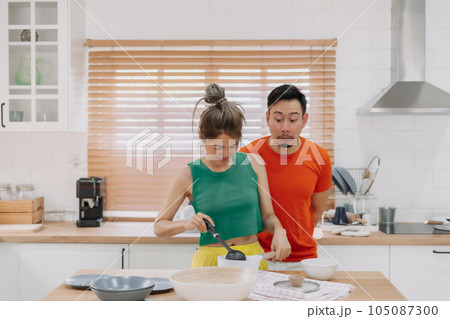 Lover couple. Funny shocked face reaction of husband looking at wife cooking. 105087300
