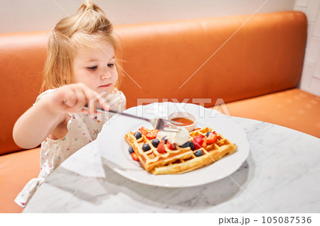 Happy 3 year old girl eat. Breakfast in cafe. Classic Viennese waffles with ice cream, berries and Maple syrup. Table in the restaurant. 105087536