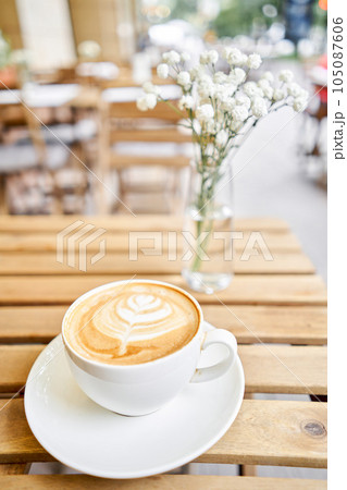 Cup of hot cappuccino. The table in the coworking space of the coffee shop. A cup of coffee on the veranda on a sunny day. Coffee break at the cafe. Close-up 105087606