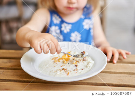 Little kid having breakfast at cafe. Adorable girl drinking still water, eating rice porridge with mango. enjoying breakfast.  105087607