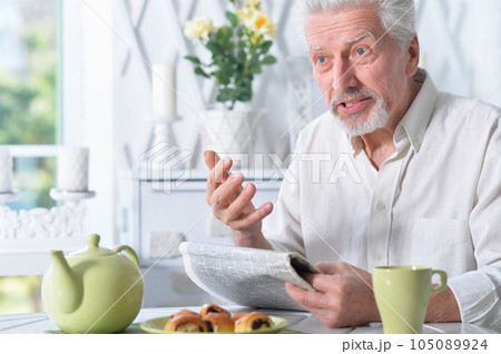 Emotional senior man reading newspaper at home Emotional senior man reading newspaper at home 105089924