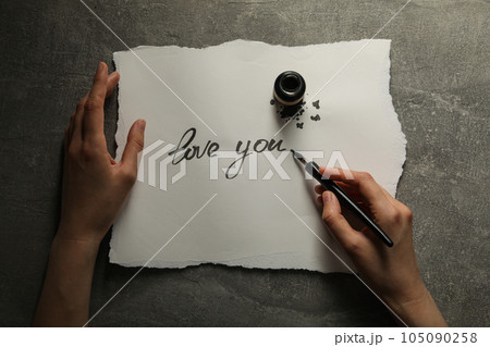 Ink bottle, pen in hand and words Love you on paper on gray background, top view 105090258
