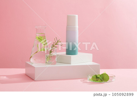 Against the pink background, a blank bottle container cosmetic placed on white podiums with glassware filled with seaweed leaves. Space for design, advertising and branding cosmetic product 105092899
