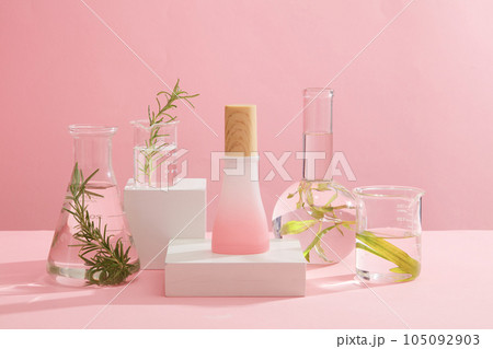Minimalist empty display product presentation scene. Cosmetic bottle unbranded on white podiums decorated with experimental flasks filled with seaweed and transparent liquid on pink background Minimalist empty display product presentation scene. Cosmetic bottle unbranded on white podiums decorated with experimental flasks filled with seaweed and transparent liquid on pink background 105092903