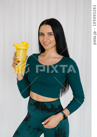 Athletic young woman holding a bottle of water after a workout at home 105093261