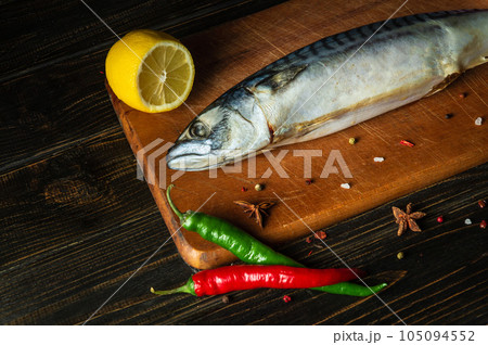 Raw mackerel or Scomber fish on kitchen cutting board before cooking with spices, pepper and lemon 105094552