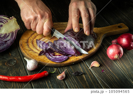 Slicing red cabbage by hands of a cook on a cutting kitchen board for preparing vegetarian food Slicing red cabbage by hands of a cook on a cutting kitchen board for preparing vegetarian food 105094565