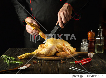 A dish of fried chicken by the hands of the chef in the kitchen of the restaurant. Before cooking, the broiler must be cut on a cutting board. Knife in the chef's hand A dish of fried chicken by the hands of the chef in the kitchen of the restaurant. Before cooking, the broiler must be cut on a cutting board. Knife in the chef's hand 105094593