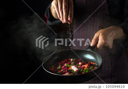 Cooking fresh vegetables. Chef adds salt to a steaming hot pan. The idea of European cuisine for a hotel with advertising space Cooking fresh vegetables. Chef adds salt to a steaming hot pan. The idea of European cuisine for a hotel with advertising space 105094610