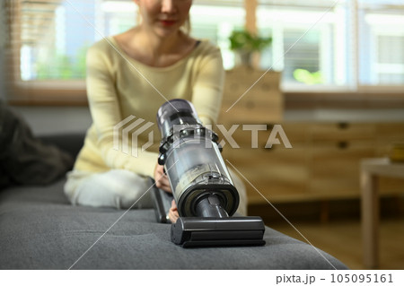 Woman vacuuming germs and dirt on couch in living room. House cleaning and housework concept 105095161