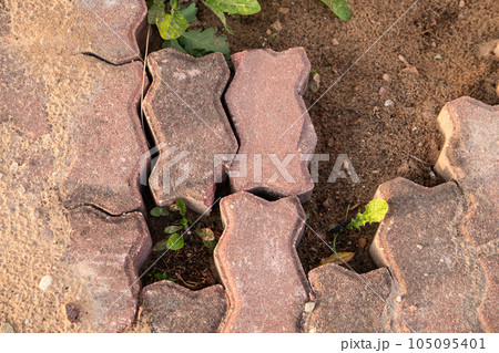 A crumbling red cobblestone road. Gravel and green grass A crumbling red cobblestone road. Gravel and green grass 105095401